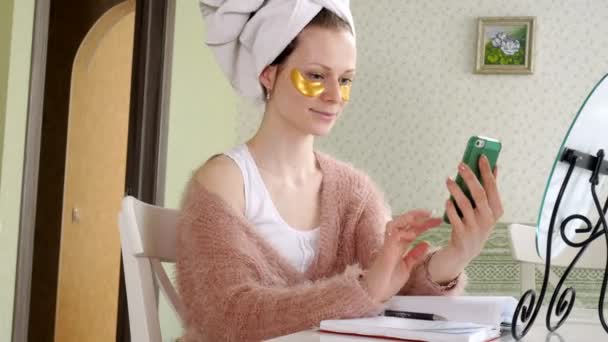 Atractiva mujer de negocios aplicando manchas faciales cosméticas en casa, hablando por teléfono — Vídeo de stock