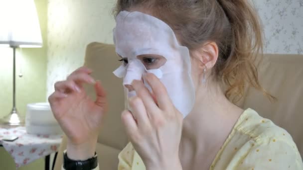 Young woman doing facial mask mask with cleansing mask on face in kitchen at home — Stock Video