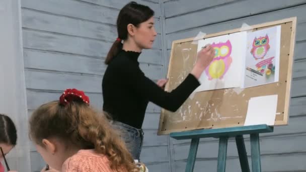 Kinderen-jongens en meisjes zitten samen rond de tafel in de klas en tekening. Met hen is hun jong en mooi leraar. — Stockvideo