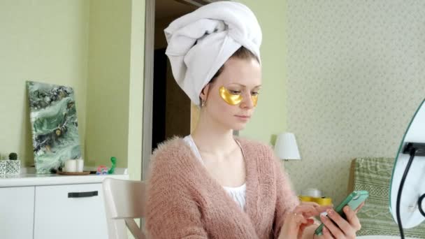 Atractiva mujer de negocios aplicando manchas faciales cosméticas en casa, hablando por teléfono — Vídeos de Stock