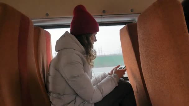 Veselá dívka v červeném klobouku, cestování autobusem na smutný den. Ona poslechu hudby — Stock video