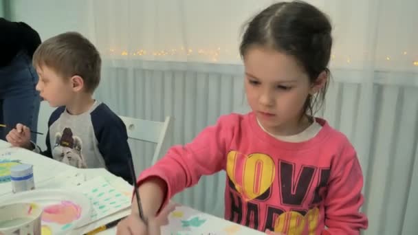 Crianças meninos e meninas sentados juntos em torno da mesa em sala de aula e desenho. Com eles está o seu jovem e belo professor . — Vídeo de Stock