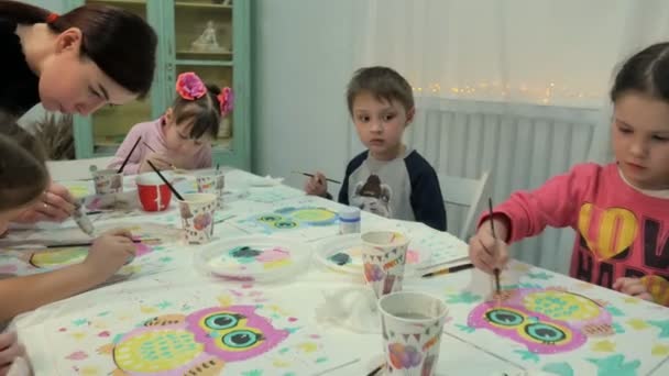 Kinderen-jongens en meisjes zitten samen rond de tafel in de klas en tekening. Met hen is hun jong en mooi leraar. — Stockvideo