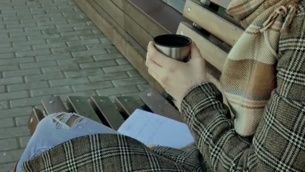 Jeune femme buvant du thé dans une bouteille thermos dans un parc de printemps assis sur un banc — Video