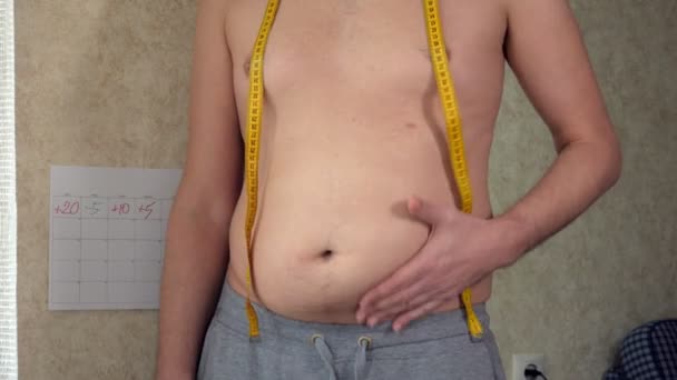 Un hombre gordo mide su cintura, una gran barriga de cerveza, un estilo de vida saludable recoge pliegues de grasa — Vídeo de stock