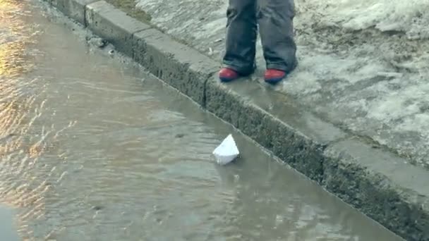 Chica en botas de goma saltando en el charco cerca de wite barco de papel — Vídeo de stock