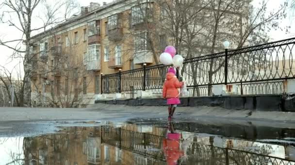 Маленькая красивая девочка прыгает на лужах после дождя — стоковое видео