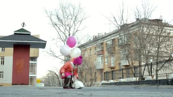 Kleines hübsches Mädchen springt nach Regen mit bunten Luftballons auf Pfützen — Stockvideo