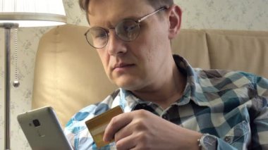 Online satın alma bir adam close-up bir telefon ve bir kredi kartı kullanan kanepede eve yaşam tarzı akıllı iş internet teknoloji banka bankacılık para tutan cep telefonu istemci closeup aygıt el alışveriş