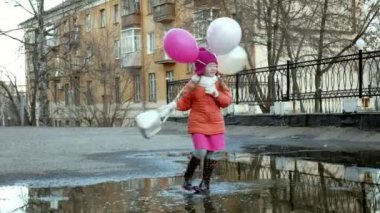 Küçük güzel kız su birikintileri üzerinde renkli balonlar ile yağmur sonra atlama