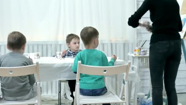 Enfants garçons assis ensemble autour de la table dans la salle de classe et le dessin. Avec eux est leur jeune et beau professeur . — Video