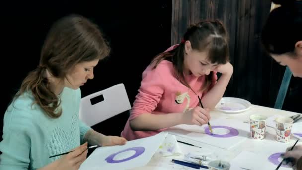 Niños niños y niñas sentados juntos alrededor de la mesa en el aula y dibujando. Con ellos está su joven y hermosa maestra . — Vídeos de Stock