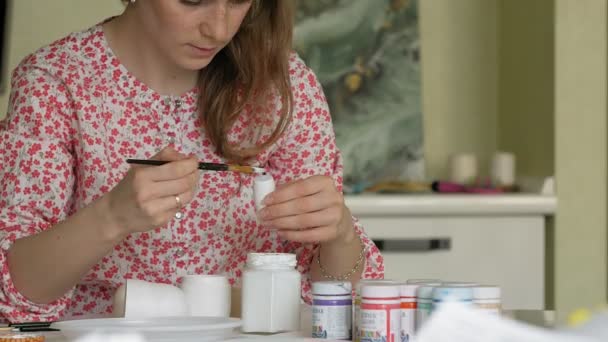 Una donna dipinge una bambola di legno con vernici colorate nel suo studio di casa, pittura Matryoshka — Video Stock