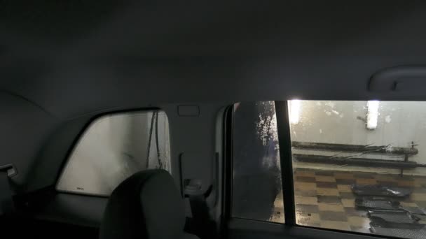 Auto passeren de car wash, een persoon wast de auto met een contactloze wastafel, een uitzicht vanaf in de auto — Stockvideo