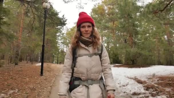 Una atractiva joven con un sombrero rojo camina por el bosque a principios de primavera con una gran mochila turística — Vídeos de Stock