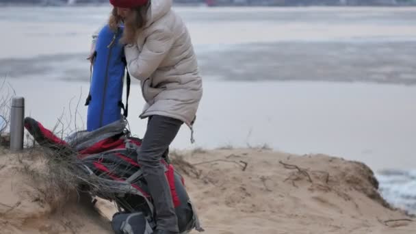 Attraktive junge Touristin mit rotem Hut sammelt ein Touristenzelt am Waldrand an der Küste — Stockvideo