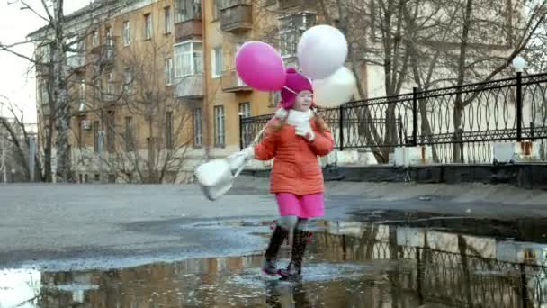 Kleines hübsches Mädchen springt nach Regen mit bunten Luftballons auf Pfützen — Stockvideo