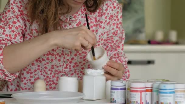 一个女人在她的家庭工作室里画一个木制的洋娃娃, 里面有彩色颜料, 俄罗斯套娃绘画 — 图库视频影像