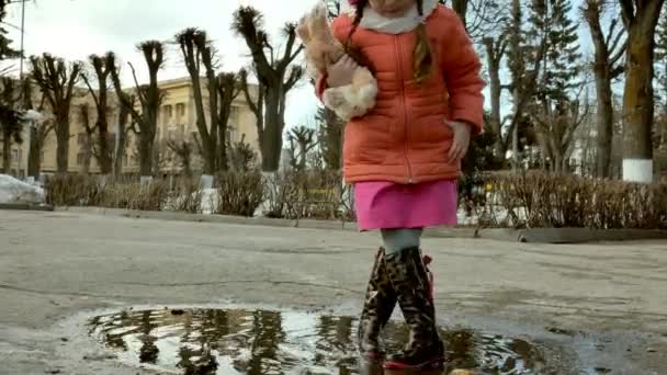 Маленькая красивая девочка прыгает на лужах после дождя — стоковое видео