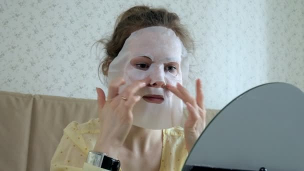 Mujer joven haciendo máscara facial con máscara de limpieza en la cara en la cocina en casa — Vídeo de stock