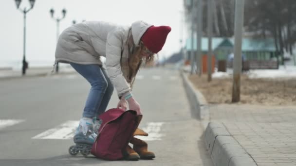 Νεαρή όμορφη γυναίκα σε ένα κόκκινο καπέλο, φορώντας σπορ ζεστά ρούχα και οδοστρωτήρες, ιππασία στο δρόμο στην ακτή — Αρχείο Βίντεο