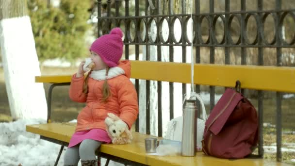 Menina bonita senta-se em um banco de parque e come uma deliciosa sobremesa — Vídeo de Stock
