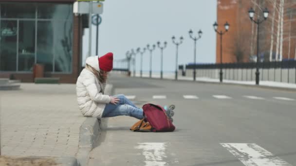 빨간 모자 입고 스포티 한 따뜻한 옷과 롤러, 아스팔트도로에 앉아 및 전화 통화에 젊은 아름 다운 여자 — 비디오