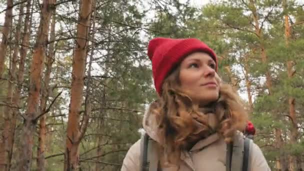 Привлекательная молодая женщина в красной шляпе гуляет по лесу ранней весной с большим туристическим рюкзаком — стоковое видео
