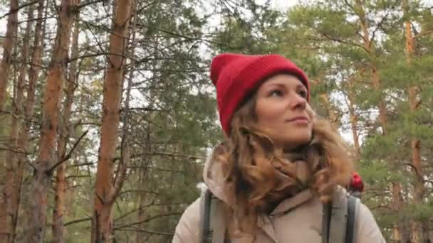 Una atractiva joven con un sombrero rojo camina por el bosque a principios de primavera con una gran mochila turística — Vídeos de Stock