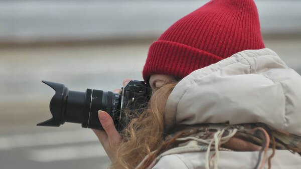 Young beautiful woman in red hat wearing sporty warm clothes and rollers, sitting on the asphalt road and taking pictures on a vintage camera