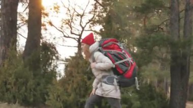 Çekici bir genç kadın kırmızı şapkalı bir büyük turistik sırt çantası ile erken baharda ormanda yürür