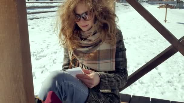 Genç bir kadın sessizce origami kağıt uçak parmakları ile dokunarak ve dizlerinin üzerinde koyarak bir ahşap verandada oturuyor. Açık havada beyaz aerogamy uçak ile oturan kız yakın görünümü, — Stok video