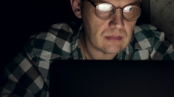 Muž v brýlích pracuje v noci. On vypadá strach, on vidí na obrazovce počítače před ním, detail — Stock video