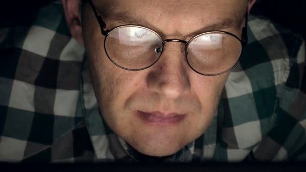 Egy férfi szemüveg működik, késő este. Úgy néz ki, zaklató, látja a számítógép képernyőjén, előtte, egy közeli — Stock videók