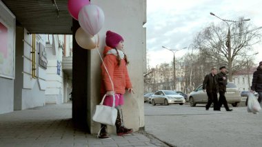 Küçük kız yürüyerek kentin erken baharda bir sokakta renkli balonlar ile