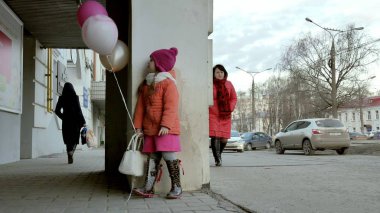 Küçük kız yürüyerek kentin erken baharda bir sokakta renkli balonlar ile