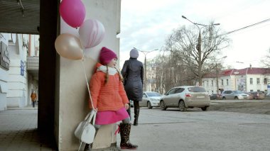 Küçük kız yürüyerek kentin erken baharda bir sokakta renkli balonlar ile
