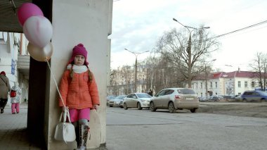 Küçük kız yürüyerek kentin erken baharda bir sokakta renkli balonlar ile