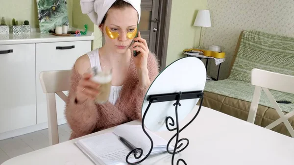 Atractiva mujer de negocios aplicando manchas faciales cosméticas en casa, hablando por teléfono —  Fotos de Stock
