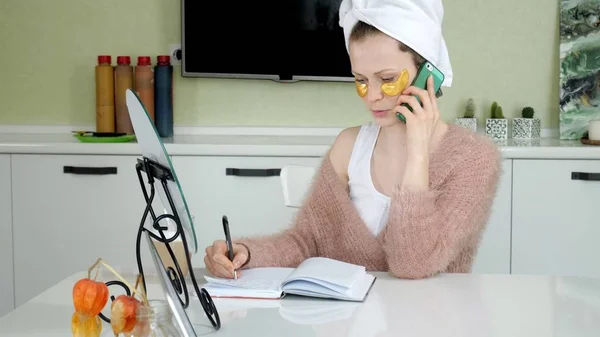 Приваблива ділова жінка застосовує косметичні плями обличчя вдома, розмовляючи по телефону — стокове фото