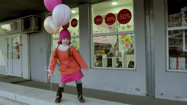 En liten flicka promenad med färgglada ballonger, på en gata i staden tidigt på våren — Stockfoto