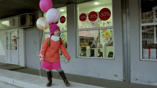 Маленькая девочка гуляет с красочными воздушными шарами, по улице в городе ранней весной — стоковое фото