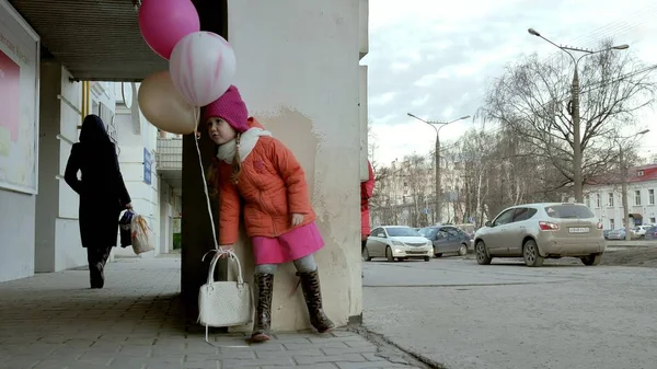 En liten flicka promenad med färgglada ballonger, på en gata i staden tidigt på våren — Stockfoto