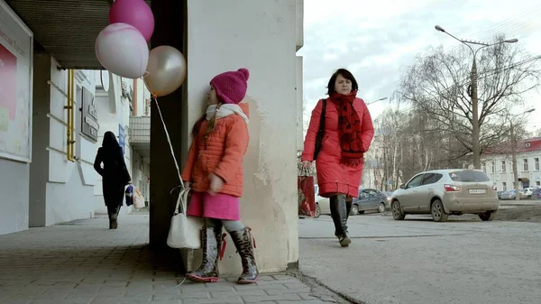 Küçük kız yürüyerek kentin erken baharda bir sokakta renkli balonlar ile