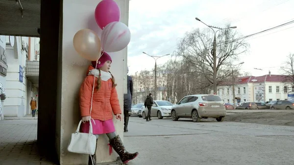 Una niña camina con globos de colores, en una calle de la ciudad a principios de la primavera —  Fotos de Stock
