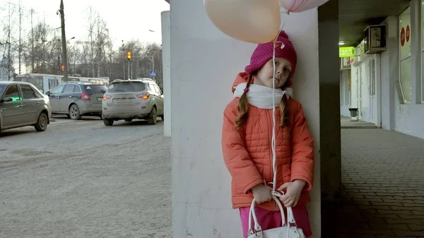 Ein kleines Mädchen spaziert mit bunten Luftballons auf einer Straße in der Stadt im zeitigen Frühling — Stockfoto