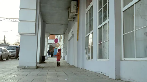 Маленькая девочка гуляет с красочными воздушными шарами, по улице в городе ранней весной — стоковое фото