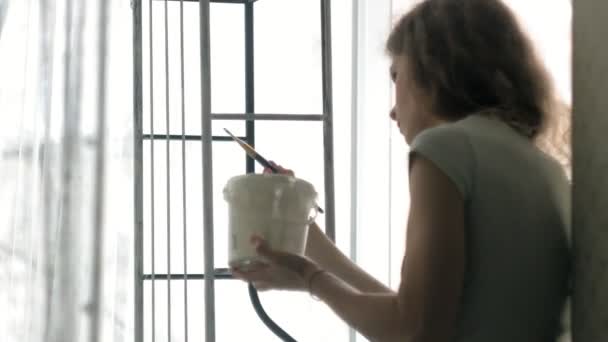 En kvinna målar svart metall möbler med en borste i vitt — Stockvideo