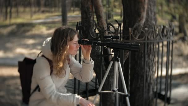 Femme attirante regarde à travers un télescope dans une forêt sur la rive de la rivière — Video