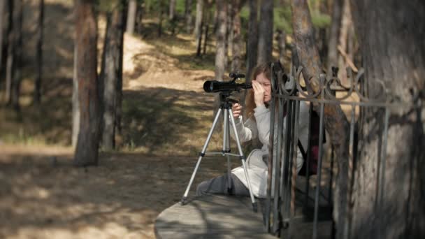 Mujer atractiva mira a través de un telescopio en un bosque en la orilla del río — Vídeo de stock